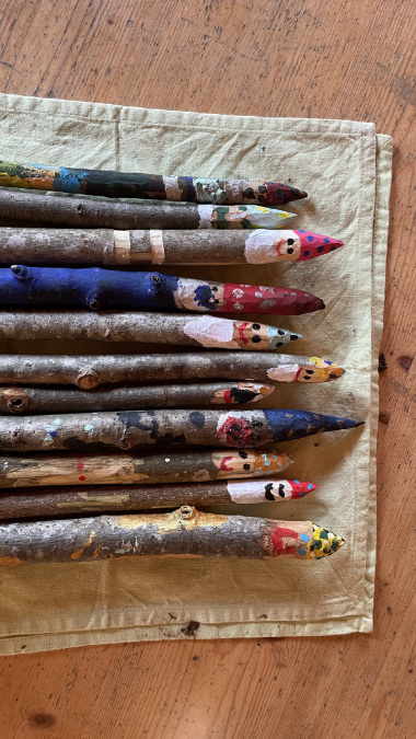 Bemalte Äste mit bunten Figuren und Mustern auf einem Tuch.