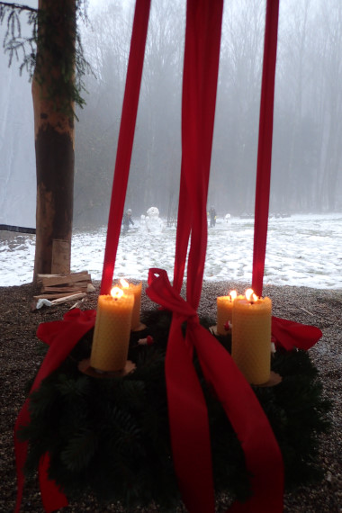 Adventskranz mit vier brennenden Kerzen vor Schneekulisse