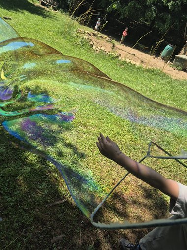 Ein Kind zieht eine riesige schillernde Seifenblase auf der Wiese.